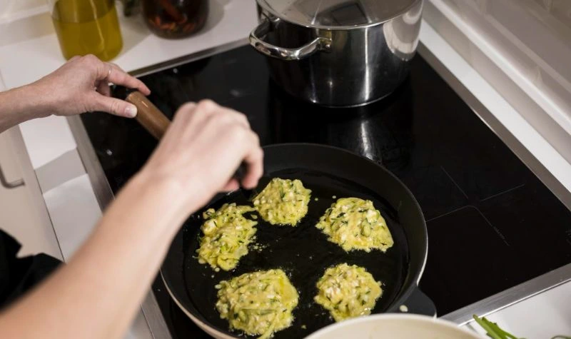 Cooktop 5 bocas a gás com mesa de vidro preta e panelas em uso